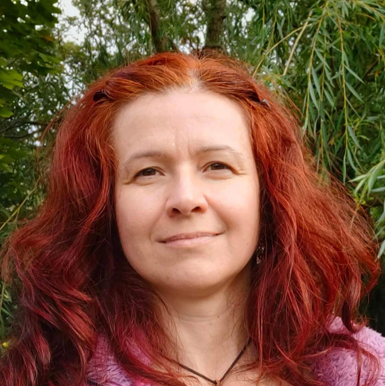 Anna Starba – instruktorka zajęć „Balans Ruch & Relax”, portret uśmiechniętej kobiety o rudych włosach na tle zieleni.