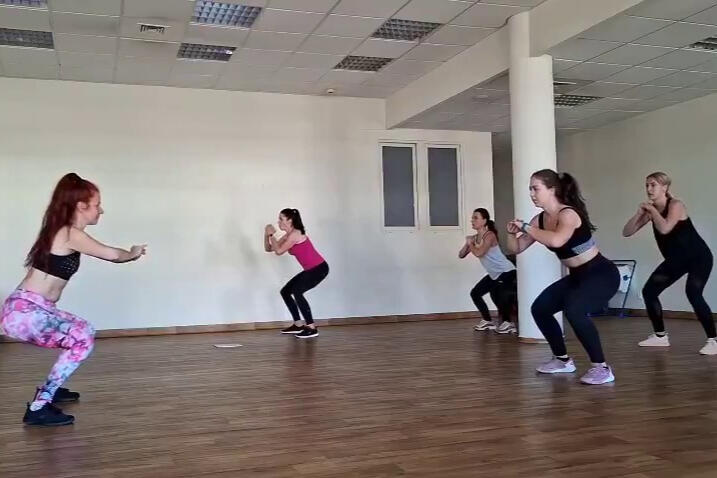 Wzmocnienie i mobilizacja kręgosłupa. Grupa kobiet wykonująca przysiady podczas treningu wzmacniającego w sali fitness pod okiem instruktorki.